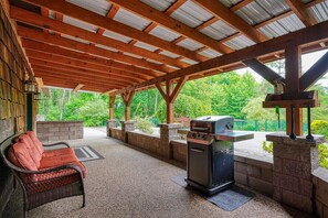 An outdoor patio with a grill, a wicker chair, and a stone wall.