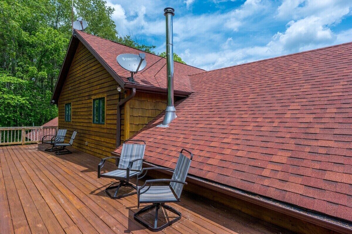 A wooden cabin with a red roof, a satellite dish, and a deck with chairs.