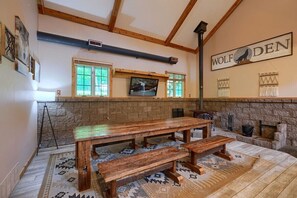 A rustic interior with a wooden table and benches, a stone fireplace, and a wall-mounted TV.