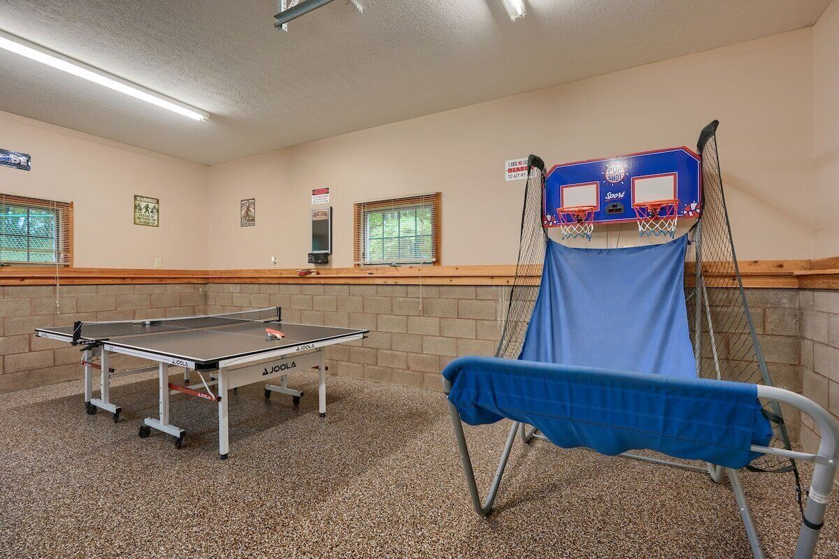 A room with a ping pong table, a basketball hoop, and a blue chair.