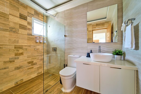 Un baño moderno con cabina de ducha de vidrio, inodoro blanco y tocador con lavamanos y espejo.