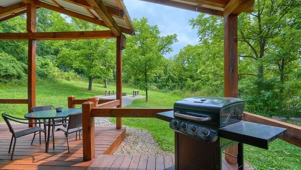 Un espacio al aire libre techado con una parrilla, una terraza de madera y una mesa con sillas.