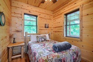 Ein Schlafzimmer einer Holzhütte mit einem Bett, zwei Fenstern, einem Nachttisch und einer Lampe.