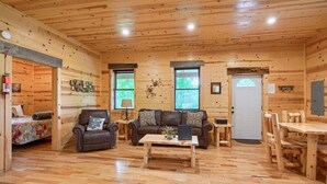 Interior de una cabaña de madera con sofá, sillón, mesa de centro y mesa de comedor.