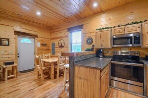 A wooden cabin interior with a dining area, kitchen with modern appliances, and a door with a frosted glass window.
