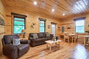 L’intérieur d’un chalet en bois, avec un canapé, un fauteuil, une table à manger et des chaises.