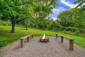 Un foyer avec des bancs, installé dans un espace herbeux entouré d’arbres.