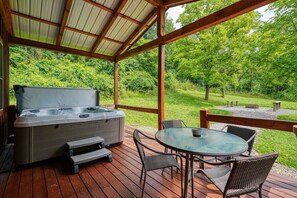 A hot tub with a wooden deck and outdoor seating area, surrounded by lush greenery.
