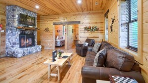 Interior acogedor de una cabaña con chimenea de piedra, paredes de madera, un sofá de cuero y una mesa de comedor.