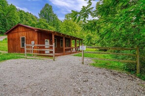 A wooden cabin with a porch, surrounded by a gravel driveway and a wooden fence.