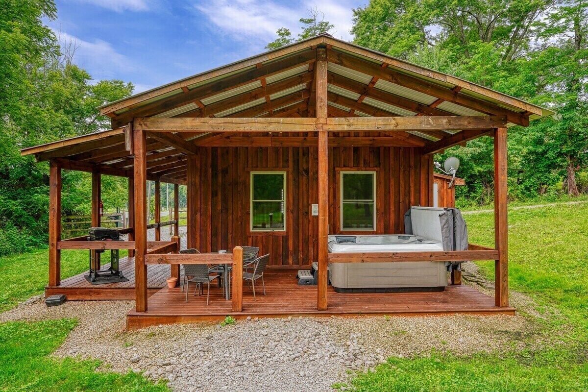 Una cabaña de madera con un porche cubierto, un jacuzzi y una mesa con sillas.