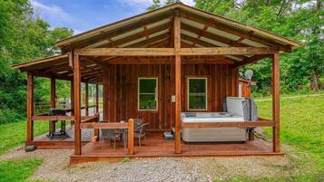 Una cabaña de madera con un porche cubierto, un jacuzzi y una mesa con sillas.