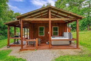Een houten chalet met een overdekt terras, een jacuzzi en een tafel met stoelen.