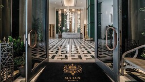 Eine luxuriöse Hotelhalle mit einem geometrisch gemusterten Boden, einer Rezeption und einem schwarzen Teppich mit dem Hotel-Logo.