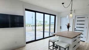 Une cuisine moderne dotée d’un grand îlot central, de meubles blancs et offrant une vue à travers la porte vitrée.