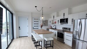 Une cuisine moderne avec des meubles blancs, un îlot central en bois, des appareils électroménagers en acier inoxydable et une grande fenêtre.