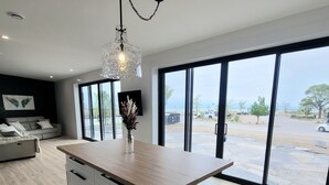 Une cuisine moderne dotée d’un grand îlot central, de meubles blancs et offrant une vue sur l’extérieur grâce à de grandes fenêtres.