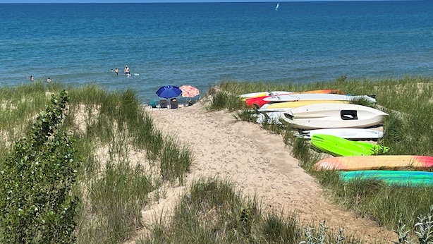 A beach with a sandy path leading to a row of colorful kayaks and a blue umbrella.