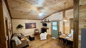 A cozy cabin interior with a wooden ceiling, a sofa, a dining table, and a chair. - Charming 2-bedroom cabin in beautiful mountains of Pickens, SC. (Pickens)