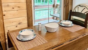 A wooden dining table with two white bowls and plates, a small bottle, and a chair. - Charming 2-bedroom cabin in beautiful mountains of Pickens, SC. (Pickens)