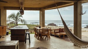 Un espace de restauration aménagé au bord de la plage, avec une table et des chaises en bois, un hamac et une vue sur l’océan.