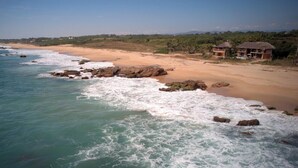 Une plage au rivage rocheux, avec une eau claire et quelques bâtiments visibles au loin.