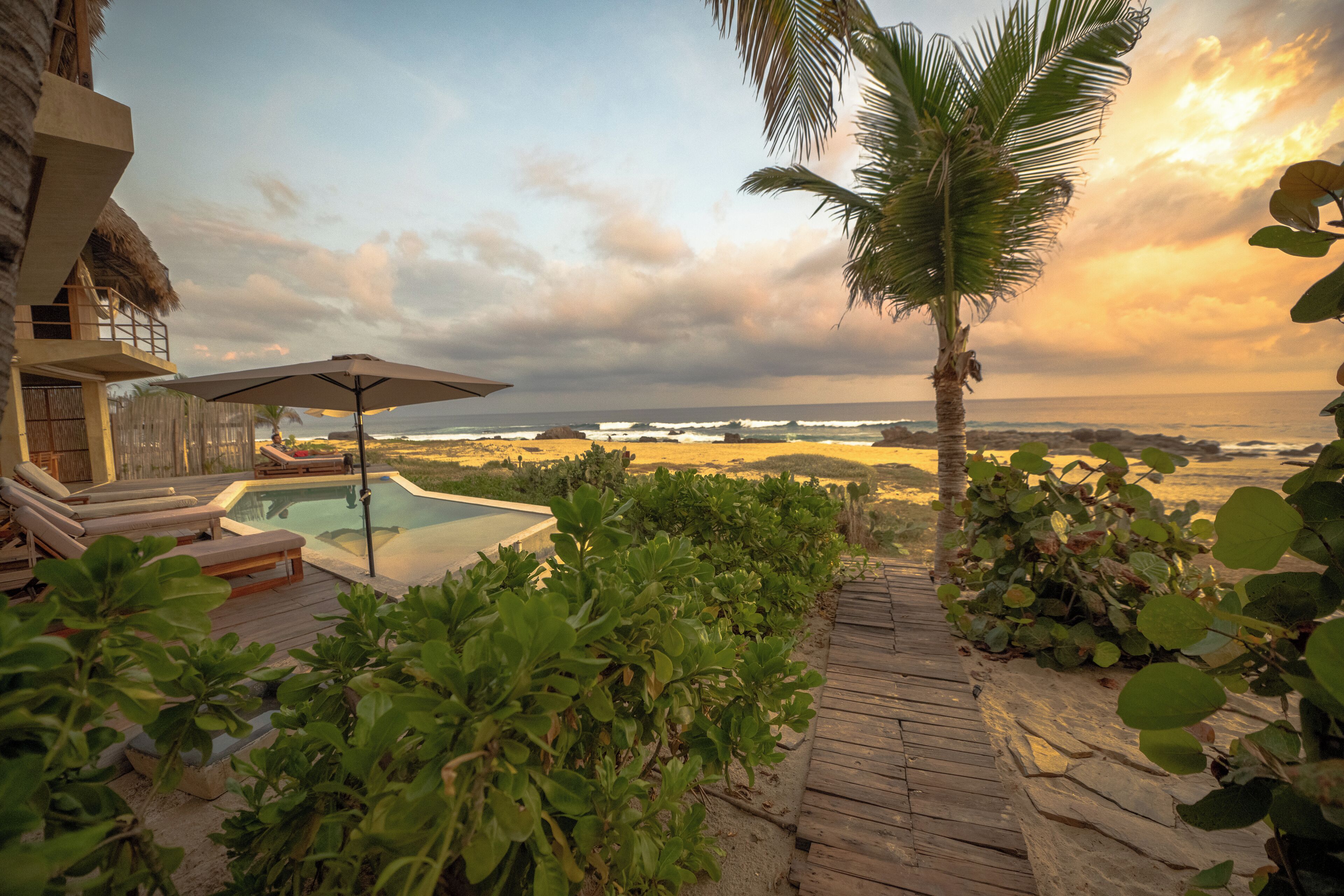 A wooden deck with lounge chairs and a pool, overlooking the ocean.