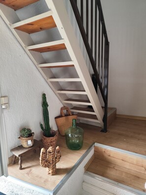 Stairs lead to an upper floor with a wicker basket, a glass bottle, and a potted plant on the landing.