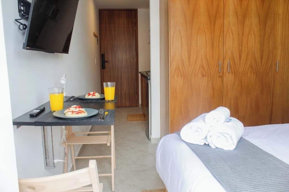 Ein Hotelzimmer mit einem Bett, einem Schreibtisch mit Stuhl, einem an der Wand montierten Fernseher und einem Holzschrank.