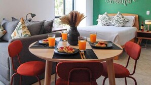Uma área de refeições com uma mesa redonda, cadeiras vermelhas e uma mesa posta para café da manhã, incluindo pratos de comida e copos de suco de laranja.