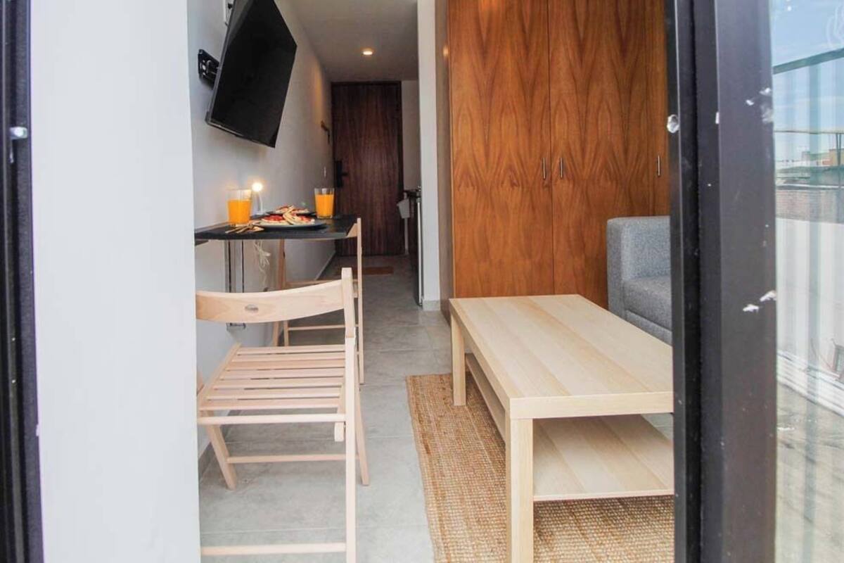 Ein gemütlicher Raum mit Holztisch und Stuhl, einem kleinen Schreibtisch ebenfalls mit Stuhl, einem an der Wand befestigten Fernseher und einem Holzschrank.
