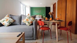 Uma sala de estar moderna com um sofá cinzento, cadeiras vermelhas, uma mesa de jantar e uma parede verde de destaque.