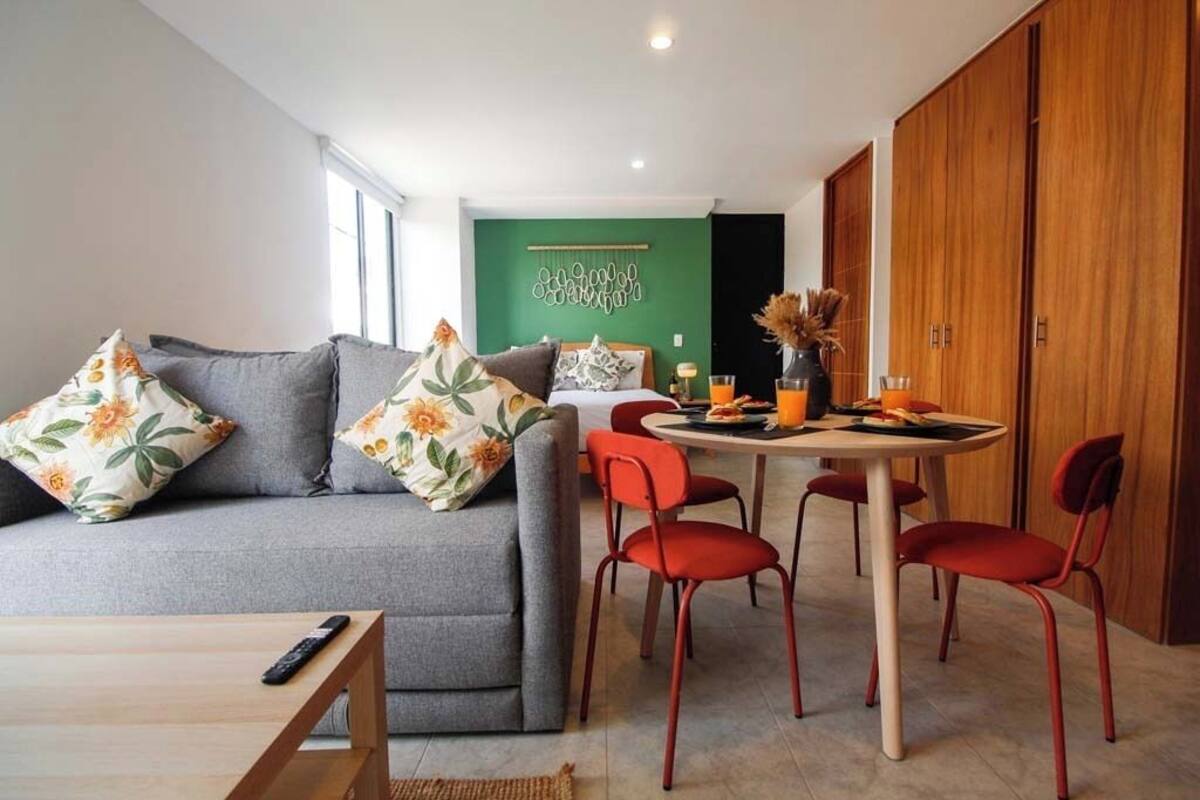 Ein modernes Wohnzimmer mit einem grauen Sofa, roten Sesseln, einem Esstisch und einer grünen Akzentwand.