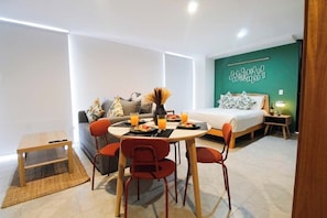 A modern room with a bed, a dining table with chairs, a small table, and a wall with a decorative light fixture. - Tribu Santa Tere (Guadalajara)