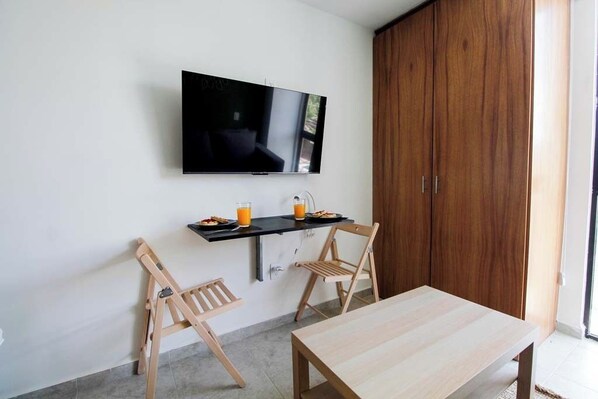 Een moderne kamer met een aan de muur bevestigde televisie, een houten tafel, twee houten stoelen en een garderobe.