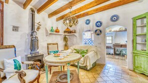 Une pièce chaleureuse avec une table ronde, un canapé et un fauteuil. Des assiettes décoratives ornent le mur, et une statue se trouve à gauche.