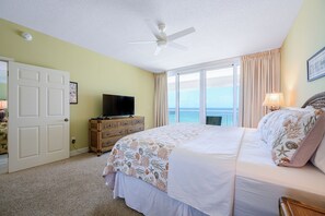 A hotel room with a bed, a television, a dresser, and a balcony with a view.