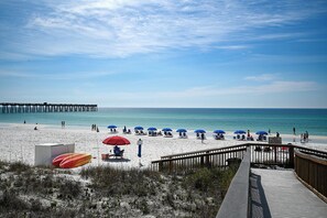 A beach with a wooden pier extending into the water, a sandy beach with umbrellas, and a wooden walkway leading to the beach.