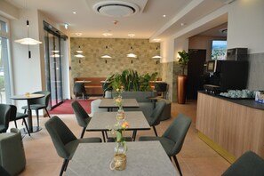En moderne hotellobby med flere siddeområder, en receptionsdisk og et stort vindue med udsigt over byen.