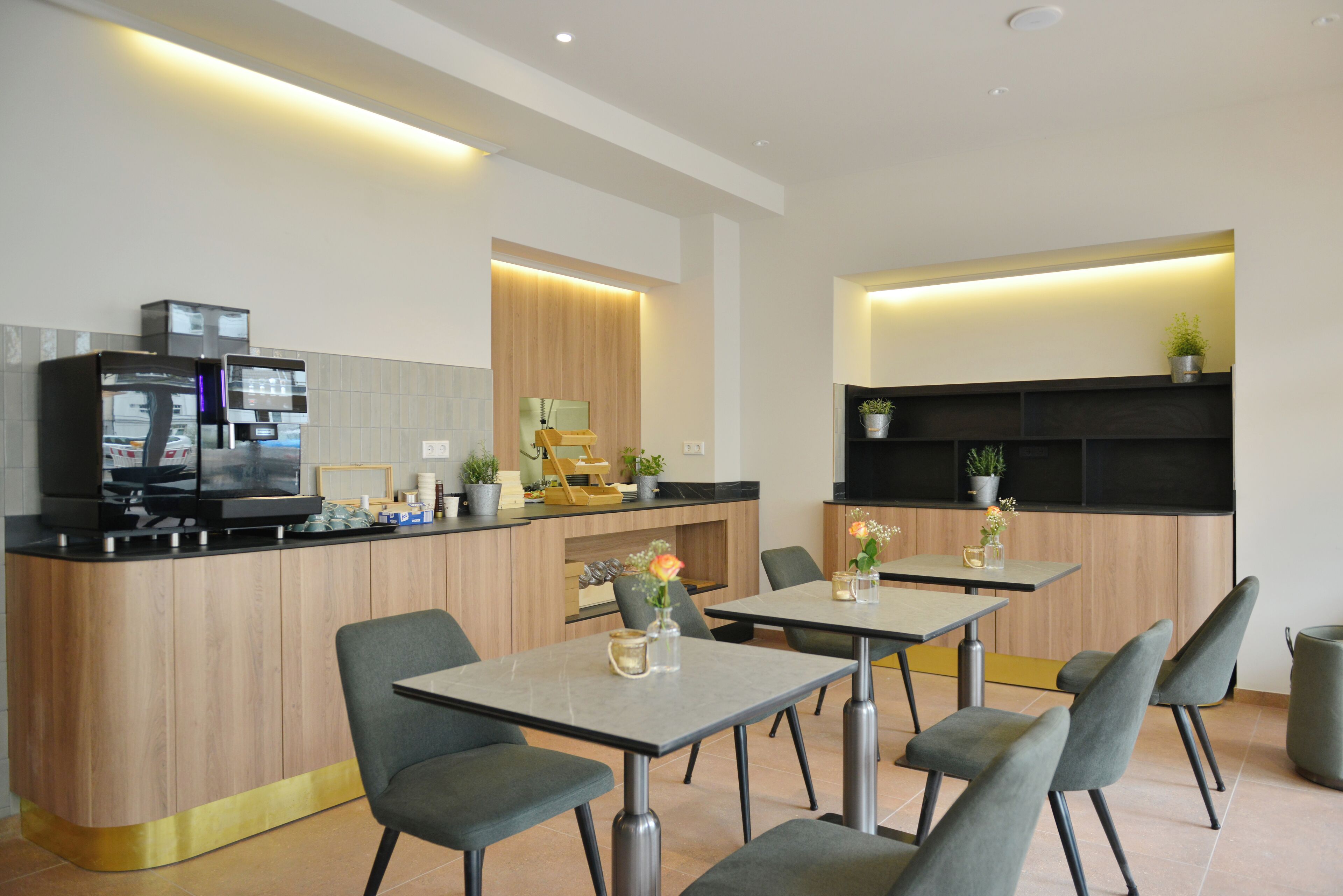 A modern kitchen with a built-in refrigerator, microwave, and coffee machine. There are two dining tables with chairs, and a small bar area with a TV.