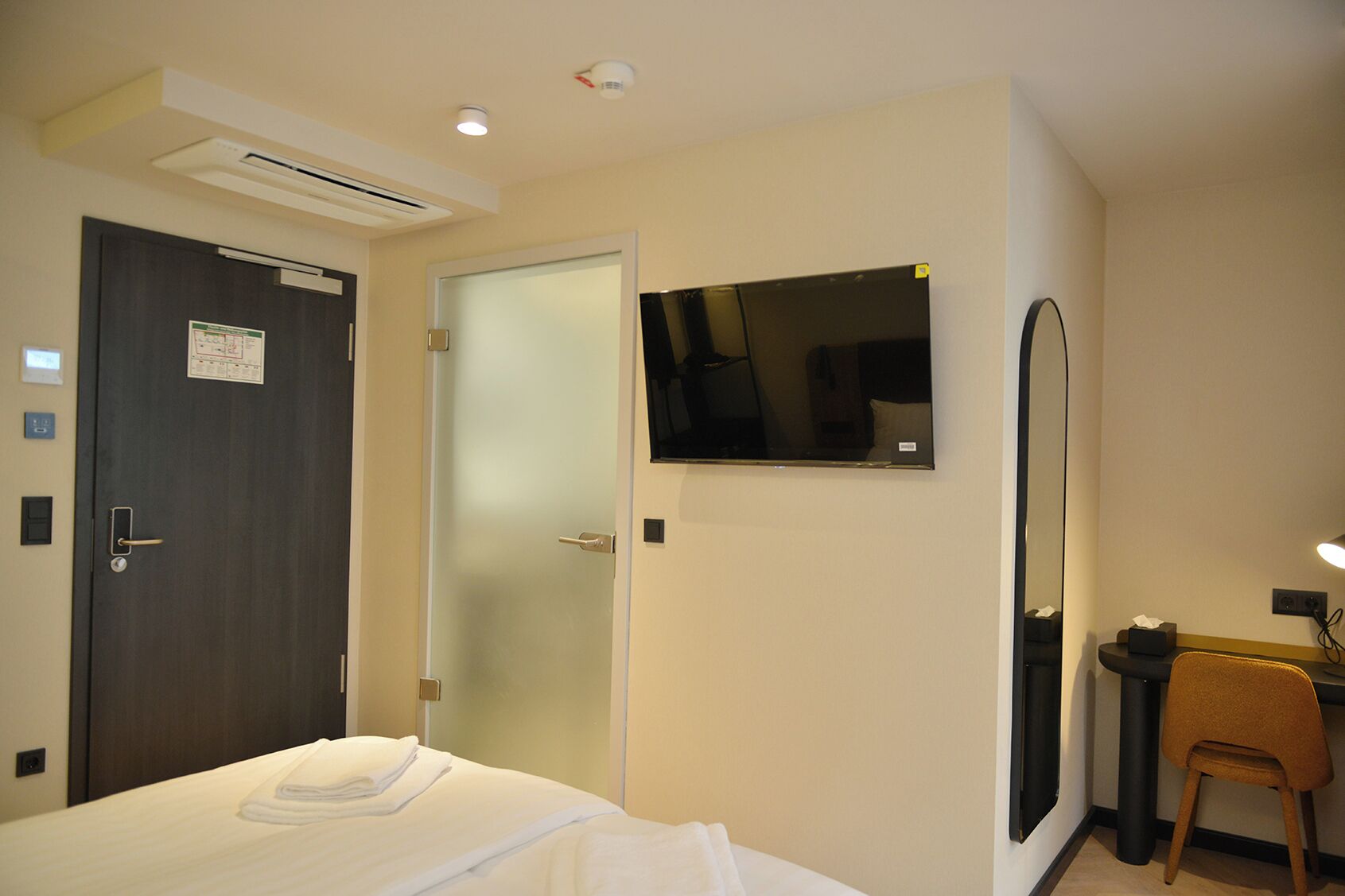Una habitación de hotel con una cama, un escritorio con una silla, un espejo y una puerta.