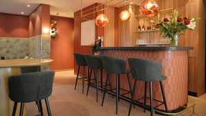 A bar area with a counter, stools, and a vase with flowers. - Day8 Hotel  (Cologne)
