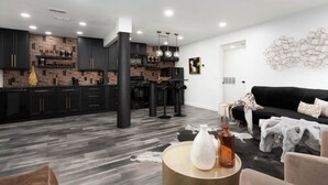 A modern kitchen with dark cabinetry and a central island, a dining area with a black table and chairs, and a living room with a black sofa and decorative pillows. - 60 day min Charlotte South Park 1bed 1bath (Charlotte)