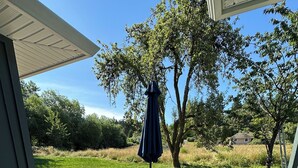 A covered outdoor patio with a table and chairs, a potted plant, and a view of the surrounding greenery. - Serene Farm Stay (Nanaimo)