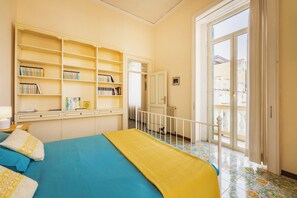 A room with a bed, a bookshelf, a desk, and a view through a door. - CasaChi | View of Capri, a balcony, and charm in the heart of Chiaia—Naples (Napoli)