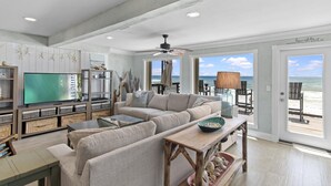 A spacious living room with a large flat-screen TV, comfortable seating, and a view of the ocean through large windows. - Green Reef #7- Emerald Horizon (Destin)
