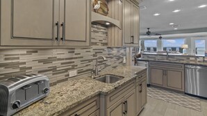 A modern kitchen with granite countertops, stainless steel appliances, and a backsplash with geometric tiles. - Green Reef #7- Emerald Horizon (Destin)