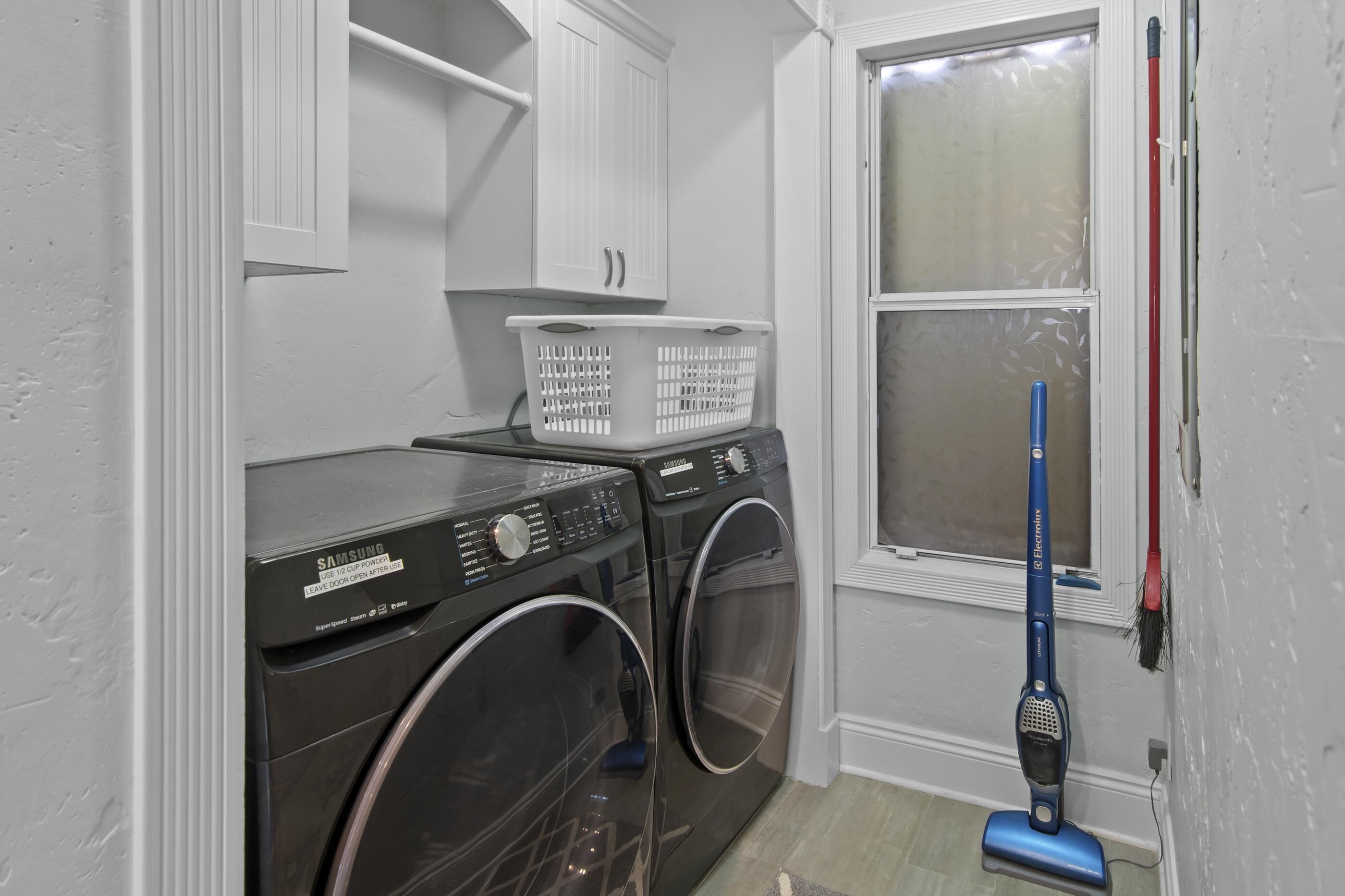 Un espace buanderie comprenant deux machines à laver à chargement frontal, un panier à linge blanc et un aspirateur bleu.