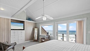 A bedroom with a large bed, a ceiling fan, a TV, a dresser, and a view of the beach. - Green Reef #7- Emerald Horizon (Destin)