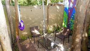 An outdoor seating area with two chairs and a table, surrounded by a chain-link fence, trees, and a colorful mural. - Casa Selva Arte Bacalar Free Bikes & Kayaks (Bacalar)